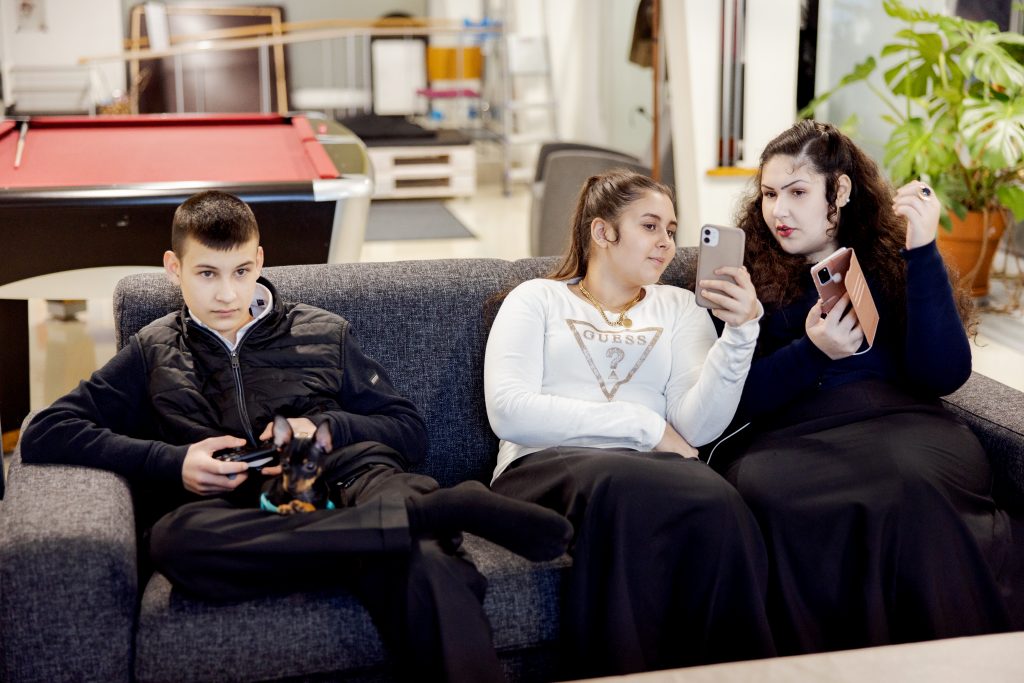 Romaninuoret istuvat sohvalla, katselevat kännykkää ja pelaavat konsolilla