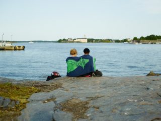 Ett par sitter bredvid varandra med handdukar över axlarna vid havet.