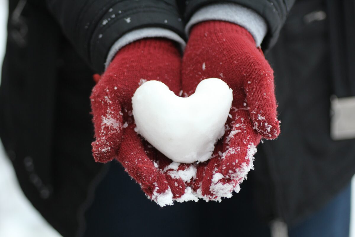 Villalapasilla puetut kädet pitelevät sydämenmuotoista lumipalloa.